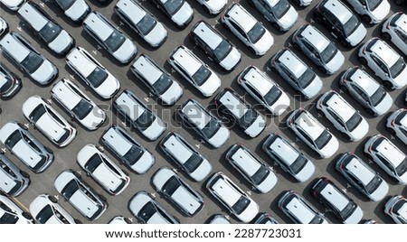 Aerial view of new cars stock at factory parking lot. Above view cars parked in a row. Automotive industry. Logistics business. Import or export new cars at warehouse. Big parking lot at port terminal