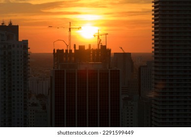 Aerial view of new developing residense in american urban area at sunset. Tower cranes at industrial construction site in Miami, Florida. Concept of housing growth in the USA