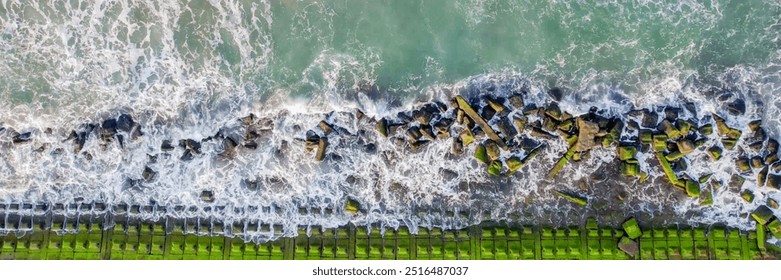 Aerial view of the ocean waves crashing against a mossy rocky shoreline, symbolizing erosion and coastal protection challenges - Powered by Shutterstock