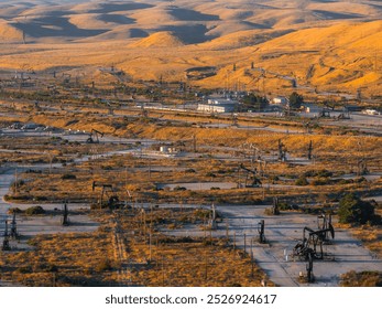 Aerial view of oil rigs and pumpjacks in a desert landscape in California. Dry hills and sparse vegetation surround the industrial scene in warm light. - Powered by Shutterstock