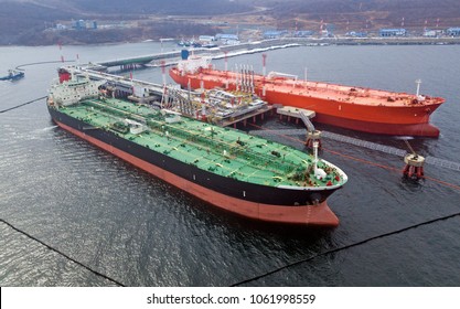 Aerial view of Oil tanker ship loading in port, Crude oil tanker ship under cargo operations on typical shore station with clearly visible mechanical loading arms and pipeline infrastructure.