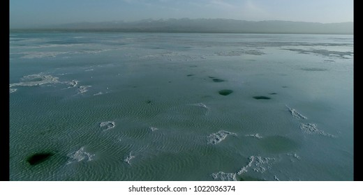 Aerial view on Chaka Salt Lake on the Tibetan Plateau showing the lake’s thick salt bed that lies close to the water surface, a blue cloudy sky and mountains in the background. Qinghai Province, China