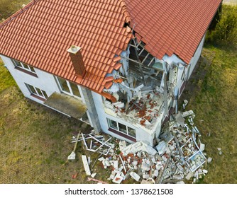 Aerial view on damaged red single house roof after strong wind or explosion. Hole in the rooftop and floor. Rubble on the ground.