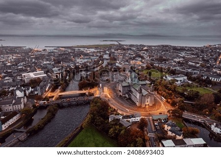 Aerial view on Galway Cathedral Building illuminated by city lights at dusk. Salmon Weir Bridge and new pedestrian bridge. Dark muted color. Galway city, Ireland. Town landmark.