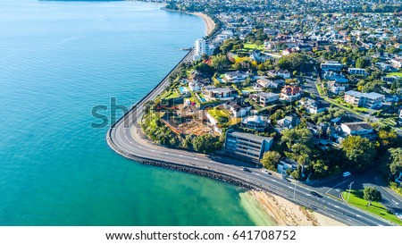 Aerial view on a road running along sea shore with residential suburbs on the background. Auckland, New Zealand.
