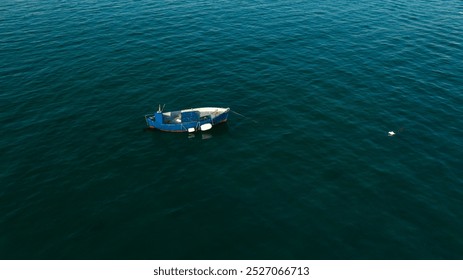 Aerial view of a one small fishing boat anchored in the middle of the sea. The boat is empty and lonely. - Powered by Shutterstock