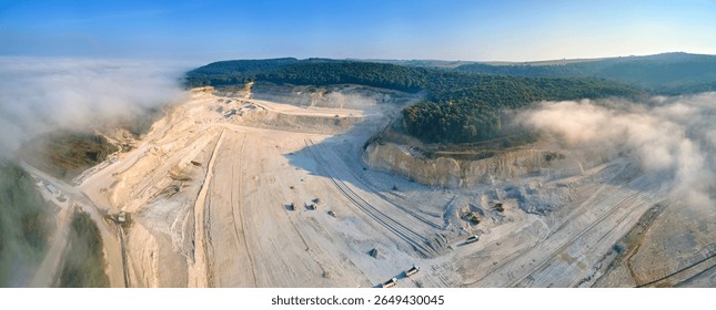Aerial view of open pit mining site of limestone materials extraction for construction industry with excavators and dump trucks.