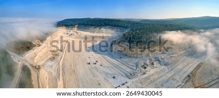 Aerial view of open pit mining site of limestone materials extraction for construction industry with excavators and dump trucks.