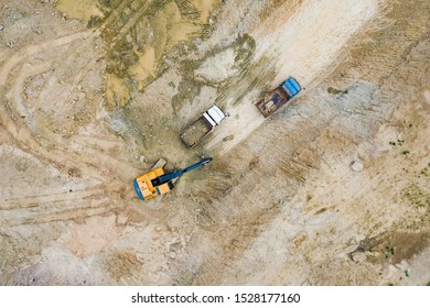 Aerial view, orange excavator with truck working in quarries site. Activity in field construction business. Heavy equipment for digging in the ground. Top view from drone.