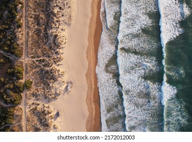 Aerial view over the clear beach and blue water of Fonte da Telha, Portugal. Top down shot of empty sandy ocean coast with huge waves
