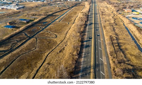 An aerial view over a dry, brown salt marsh on Long Island, NY. A multilane road runs through it, taken on a sunny, cold day with only a few cars driving by.