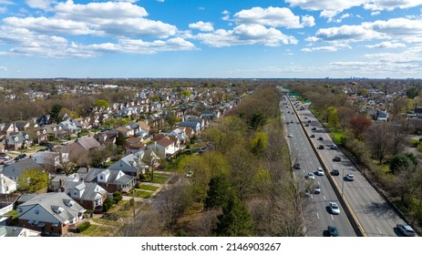 An aerial view over a long paved road during a sunny day with white clouds and blue skies. The road cuts straight through a residential neighborhood on Long Island, NY.