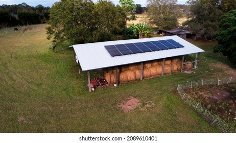 Aerial View Over North Florida Hay Barn With Cows In Background Stacked Hay Bales And Broken Down Red Tractor With Metal Roof And Renewable Solar Panels On Roof 