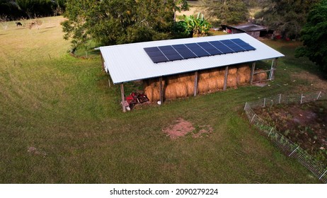 Aerial View Over North Florida Hay Barn With Cows In Background Stacked Hay Bales And Broken Down Red Tractor With Metal Roof And Renewable Solar Panels On Roof 