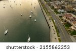 An aerial view over Sheepshead Bay, Brooklyn during a golden sunrise with boats anchored in the water. The drone camera is facing east towards the sun in a beautiful and cloudy, gold sky.