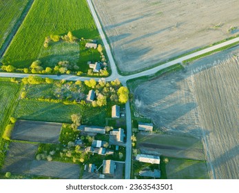 Aerial view over a small village near a dirt road. Large multi-colored fields planted with various agricultural crops. Wheat field from a bird's-eye view.