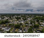 An aerial view over a suburban neighborhood on Long Island, New York with plenty of green trees under cloudy sky