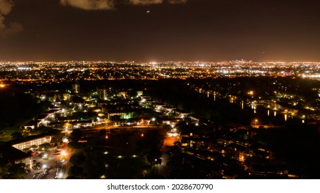 An Aerial View Over A Suburban Neighborhood At Night In Florida. There Are Colorful Street Lights And A Dark Canal. The Sky Is Clear With Some White Clouds.