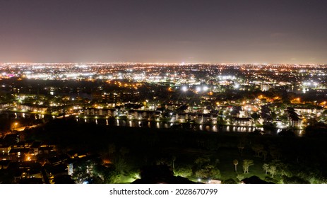 An Aerial View Over A Suburban Neighborhood At Night In Florida. There Are Colorful Street Lights And A Dark Canal. The Sky Is Clear With Some White Clouds.