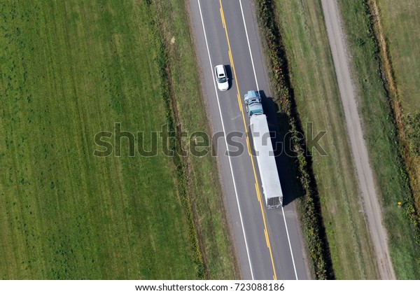Aerial view over a transport truck and a small\
car passing each other along a small country side road in rural\
Quebec, Canada.