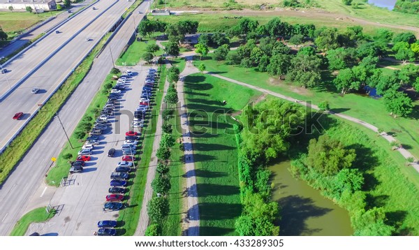 Aerial view of park entrance next to\
highway in Houston, Texas, US. Also visible is a lake side walking\
trail surrounded by green trees, warm morning light.Urban\
recreation, healthy\
lifestyle.Panorama