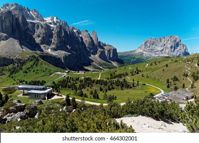 Aerial view of Pass Gardena on a sunny summer day with rugged Sella & Sassolungo mountains in background, highways & hiking tracks through the green grassy valley in Dolomiti, South Tyrol, Italy