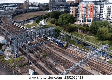 An aerial view of a passenger train travelling through a major rail junction with overhead gantry signals that have been annotated with letters to help train drivers