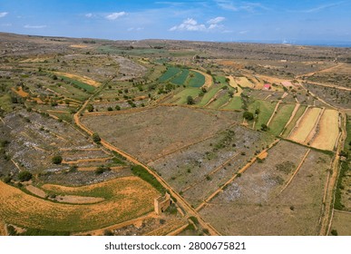 Aerial view of patchwork terraced fields surrounding La Iglesuela del Cid, with a ruined medieval watchtower at dry-stone boundary crossroads, wind turbines on horizon