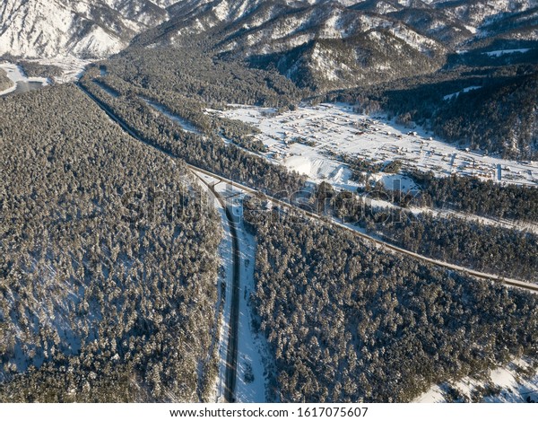 Aerial view of the paved road turning left\
with a crossroads in the mountains with conifers in winter with\
snow. Picturesque places and\
landscapes.