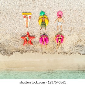 Aerial view of people lying on inflatable pineapple, pizza, star, donut, flamingo shaped mattresses on beach. Stock Photo
