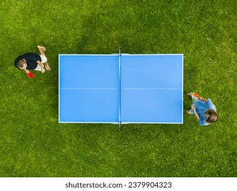 Aerial view people teenage boys  playing ping pong match outdoor. Top view two boys playing table tennis (pingpong) on a green grass lawn. Aerial view outdoor sport
						