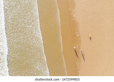 Aerial view of people walking and their shadow on a sand beach next to the waves in Porthcawl Wales UK - Powered by Shutterstock