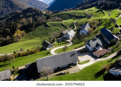 Aerial view of a picturesque mountain village nestled amidst rolling green hills, showcasing traditional farmhouses and winding roads during the autumn season. Saint Tomas village Slovenia - Powered by Shutterstock