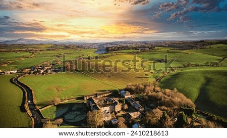 Aerial view of a picturesque rural landscape at sunset with vibrant green fields, a small village, and a winding road.