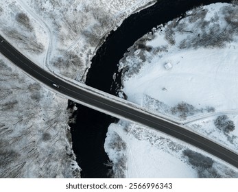 Aerial view of Pirita River in Tallinn, Estonia, during winter. Featuring a snow-covered landscape, a sleek black road bridge crossing the winding river. A lone car is driving on the road. - Powered by Shutterstock