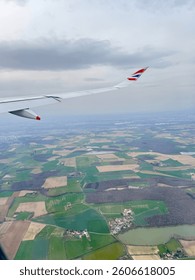 An aerial view from a plane shows patchwork fields forest and a village below. Window view from British airways.