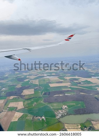 An aerial view from a plane shows patchwork fields forest and a village below. Window view from British airways.