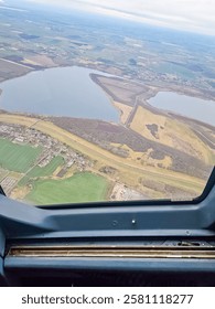 Aerial view from plane window: patchwork fields, lake, and small town under sky. High quality photo