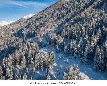 Aerial view of power line through alpine valley in Switzerland. Snow covered trees in winter. Concept of power transmission.