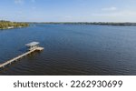 Aerial view of a private dock with boat lift with roof on a blue waterfront at Navarre, Florida. Panorama of blue waterfront in a neighborhood at Navarre with blue skyline background.