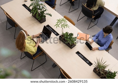 Aerial view of  professionals using laptops and tablets in a shared workspace, highlighting diversity and collaboration in a modern office environment