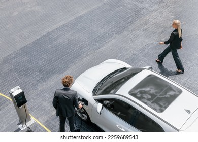 Aerial view progressive lifestyle of businesspeople with electric car connected to charging station at city center public parking car. Eco friendly rechargeable car powered by alternative clean energy - Powered by Shutterstock