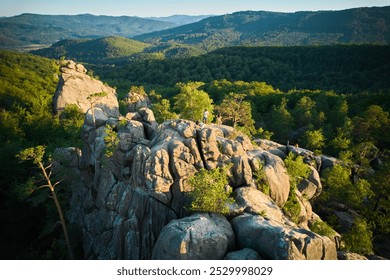 Aerial view of prominent rock formation amidst dense forest. Rolling hills and distant mountain ranges create breathtaking backdrop. Dovbush Rocks, Carpathian mountains, Ukraine. - Powered by Shutterstock