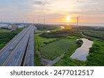 Aerial view of Provincial Highway No. 61 (West Coast Expressway) at sunset and a row of wind turbines along the seashore under golden twilight sky, in Guanyin Industrial Park, Taoyuan, Taiwan