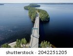 Aerial view of Pulkkilanharju Ridge road, 8 km line of islands, part of Paijanne National Park. Blue lake, road and green forest from above on a sunny summer day in Asikkala Finland.