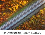 Aerial view of railroad in beautiful forest at sunset in autumn. Industrial landscape with railway station, trees with orange leaves in fall. Top view of rural railway platform. Transportation