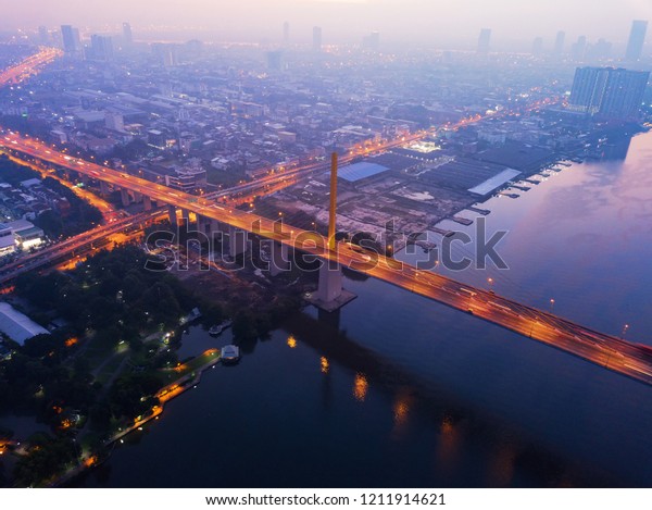 Aerial view of Rama 9 Bridge and\
Chao Phraya River in structure of suspension architecture concept,\
Urban city, Bangkok. Downtown area at sunset,\
Thailand.