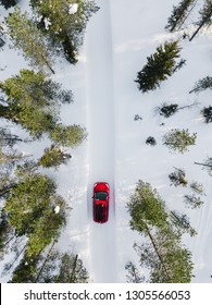 Aerial View Of Red Car Driving Through The White Snow Winter Forest On Country Road In Finland, Lapland. Top View From Drone