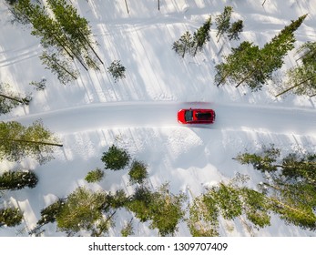 Aerial View Of Red Car Driving Through The White Snow Winter Forest On Country Road In Finland, Lapland. Top View From Drone