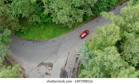 Aerial View Of Red Car Driving On Country Road In Forest. Shot From Drone Flying Over Road In Autumn Forest